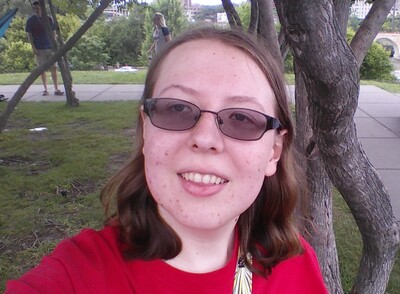A selfie of Anna in a park, with grass and trees in the background.