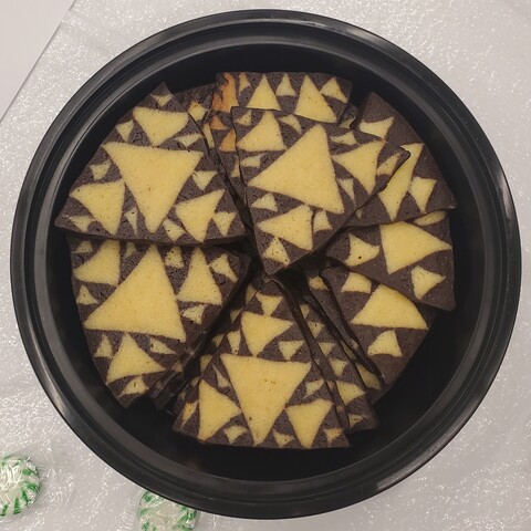 A lot of triangular cookies fit into a round container. Each cookie is a yellow and brown Sierpinski triangle; some with 3 iterations and some with just 2.