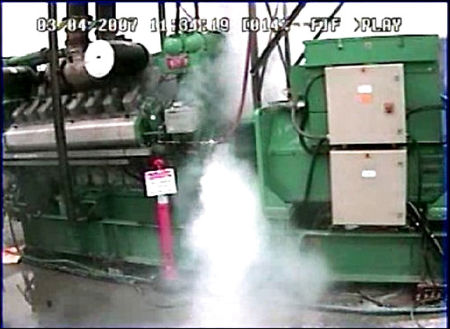 This is a picture, taken from a video of a generator that has been destroyed as part of a controlled cybersecurity test. A great amount of white smoke or steam can be seen emanating from the center of the generator.  The generator itself appears to be the size of a small bus.