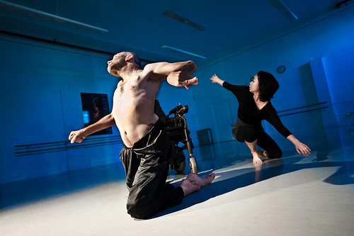 two dancers moving  in front of  powerchair in dance studio