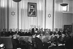 David Ben Gurion pronouncing the Declaration of the State of Israel, May 14, 1948. Tel Aviv, Israel, beneath a large portrait of Theodore Herzl, founder of modern political Zionism.